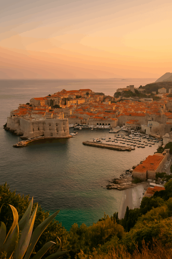 A high-resolution photograph of Dubrovnik’s coastline showing terracotta rooftops, stone walls, and the Adriatic Sea under bright summer skies.